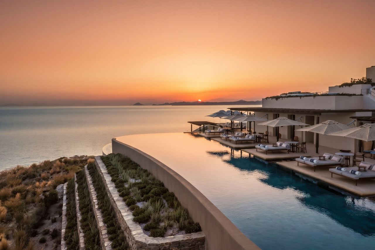 Mehrstufiger Infinity-Pool mit Liegen und Sonnenschirmen vor der Meereskulisse bei Abendrot.