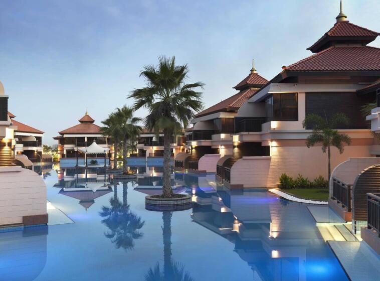 Das Anantara The Palm Dubai Resort zeigt luxuriöse Villen direkt am großen Pool, umgeben von Palmen, mit asiatisch inspirierten Dächern und eleganter Abendbeleuchtung.