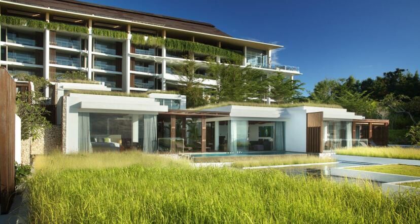 Blick auf das Anantara Uluwatu Bali Resort mit modernen Suiten und Villen, eingebettet in üppiges Grün und mit privaten Pools sowie großzügigen Glasfronten.