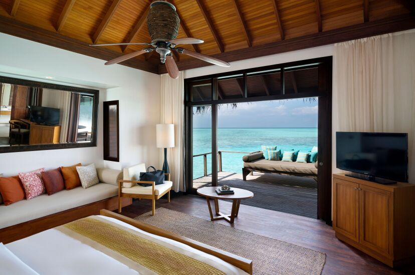 Innenansicht einer Overwater-Villa im Anantara Veli Maldives Resort mit stilvollem tropischem Interieur, Blick auf das türkisfarbene Meer und direktem Zugang zur privaten Terrasse mit Daybed über dem Wasser.