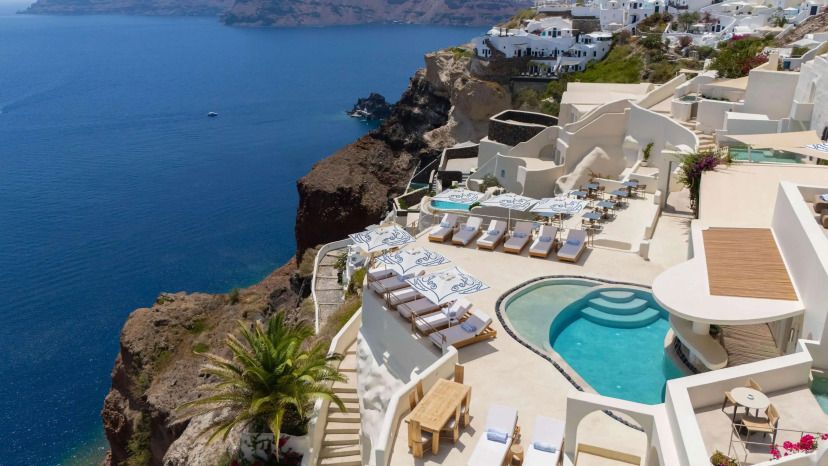 Blick auf das luxuriöse Andronis Boutique Hotel auf Santorin mit seinen in den Felsen gebauten Terrassen, eleganten Pools und spektakulärer Aussicht auf das tiefblaue Meer und die Caldera.
