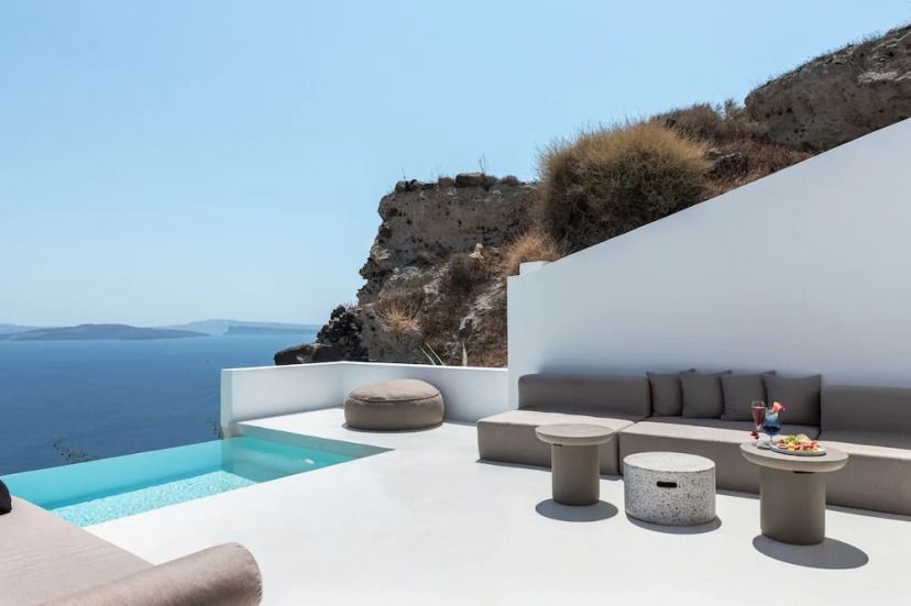 Private Terrasse der Andronis Luxury Suites auf Santorin mit Infinity-Pool, stilvollen Lounge-Möbeln und weitem Blick über die tiefblaue Ägäis und vulkanische Inseln im Hintergrund.