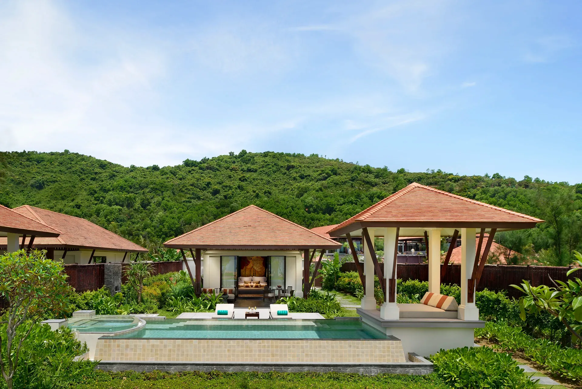 Tropische Villa des Banyan Tree Lang Co Resorts in Vietnam mit privatem Pool, offenen Pavillons und traditionellen Ziegeldächern, eingebettet in üppig grüne Natur und umgeben von bewaldeten Hügeln unter klarem, blauem Himmel.